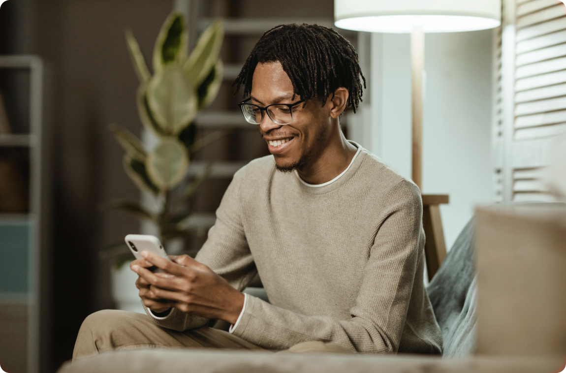 Homem com moletom bege mexendo no celular e sorrindo